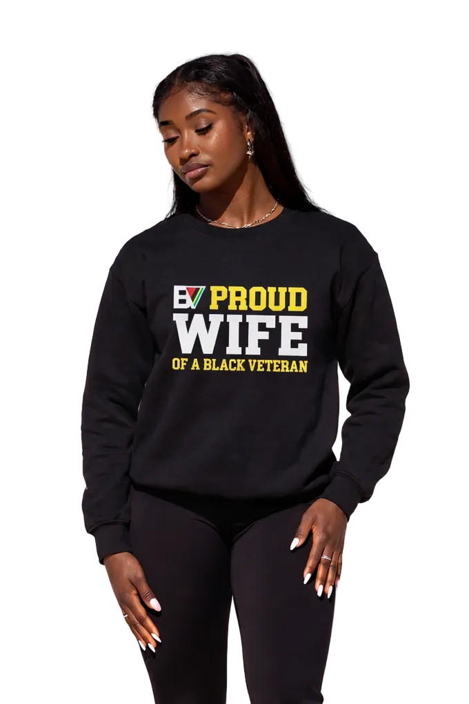 A woman wearing a black crewneck sweatshirt with the text 'PROUD WIFE OF A BLACK VETERAN' printed on the front in white and yellow, posed against a solid white background.
